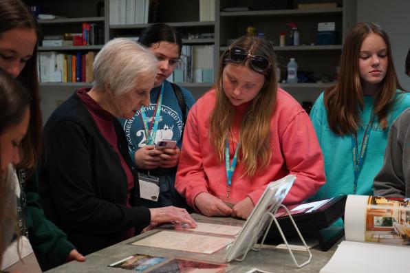Frances Gimber, RSCJ, and students gather around documents and records related to Grand Coteau held at the archives.
